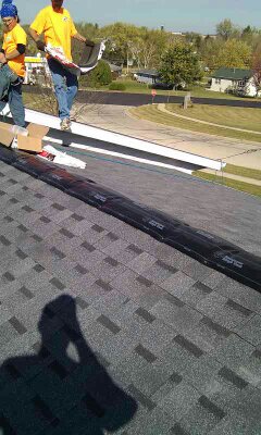 Roofing crew loading shingles and ridge vent onto a residential roof