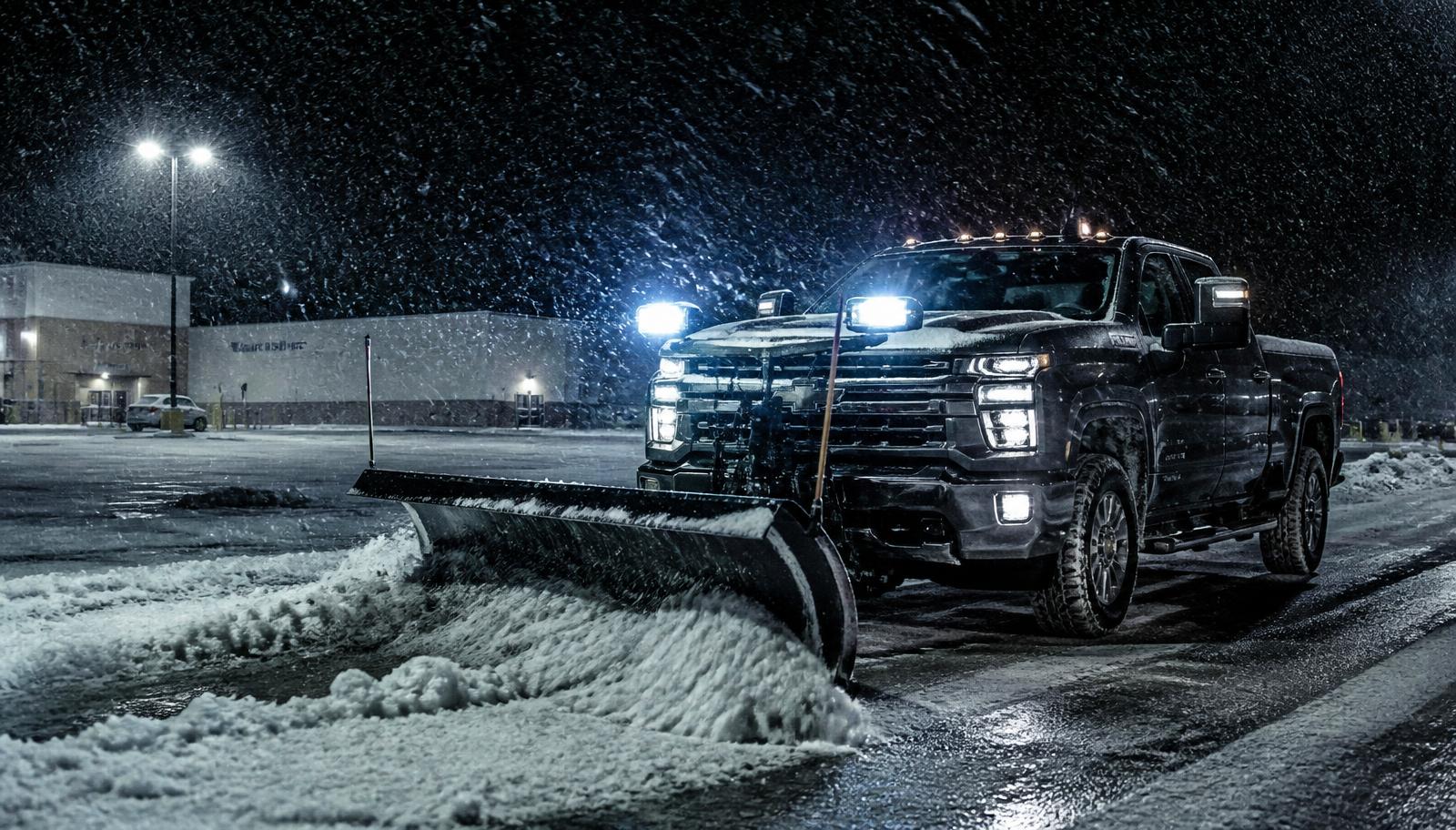 Plow truck clearing a commercial parking lot during a night snowstorm